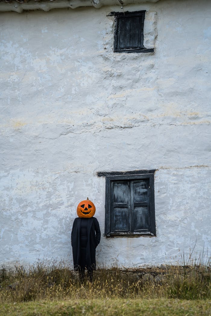 A person with a pumpkin head stands against a rustic wall in Guasca, Colombia, creating a spooky Halloween vibe.