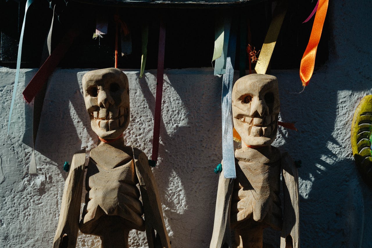 Two wooden skeleton puppets hanging with colorful ribbons, casting shadows on a sunlit wall.